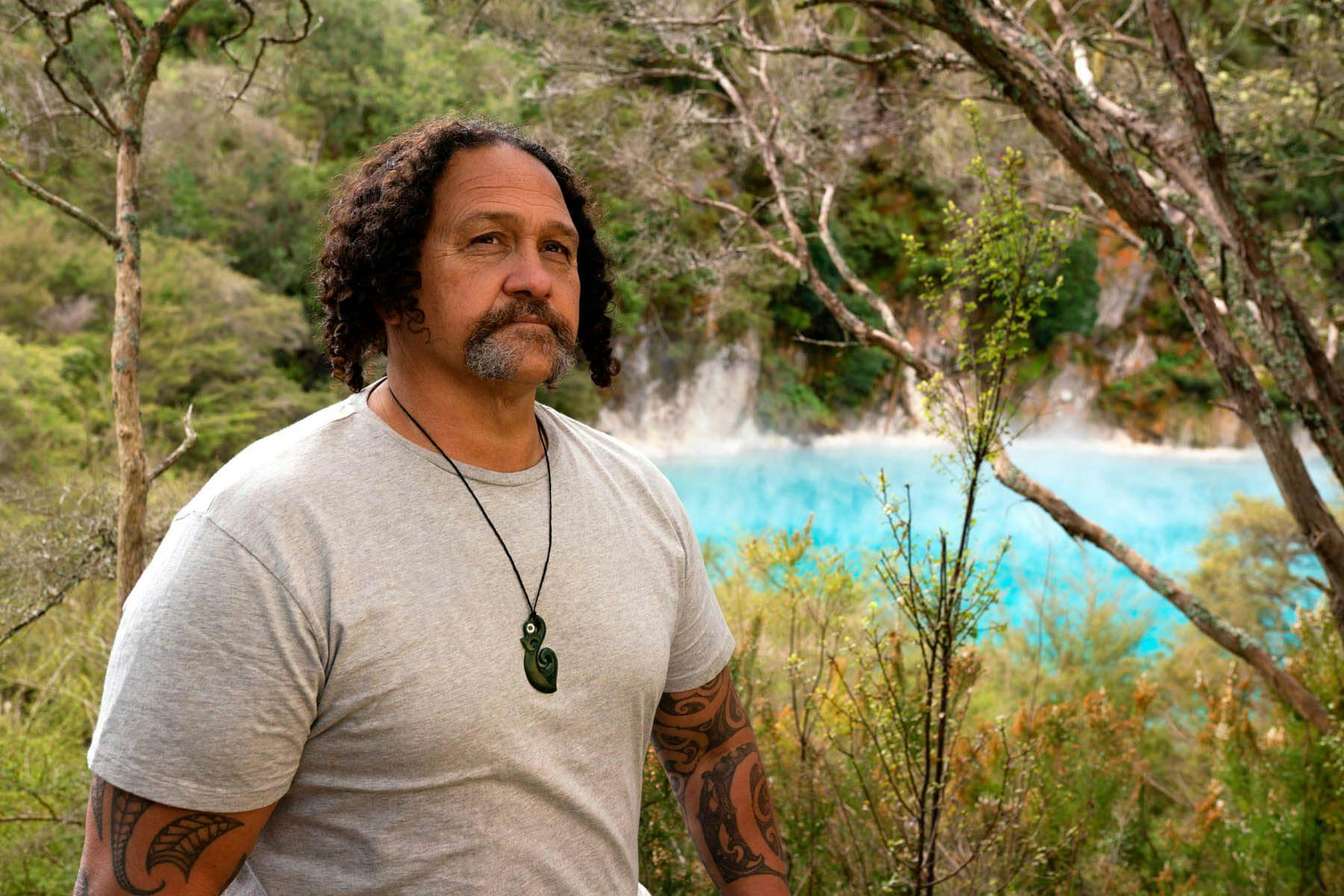 Man wears Manaia with paua eyes beside geothermal landscape