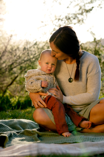 Woman wearing a koru necklace with a baby on a blanket